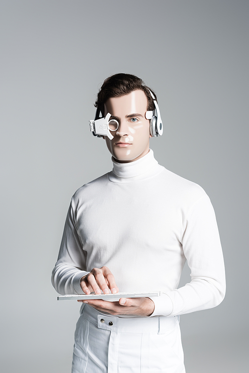 Cyborg in headphones and digital eye lens holding computer keyboard and  isolated on grey