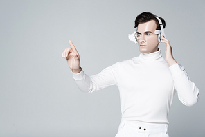 Cyborg man in headphones touching something and looking away isolated on grey