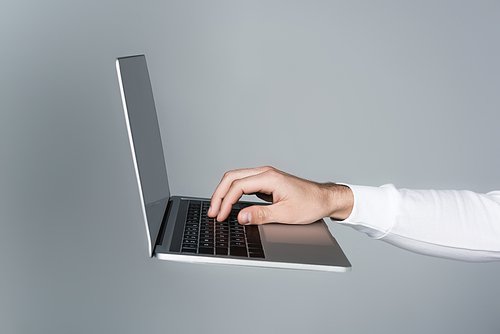 Cropped view of man using laptop with blank screen in air isolated on grey