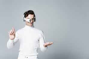 Cyborg in headphones touching and pointing at something isolated on grey