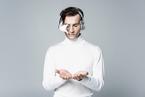 Cyborg in digital eye lens and headphones holding something on hands isolated on grey