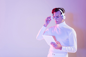 Cyborg in headphones and digital eye lens holding digital tablet on purple background