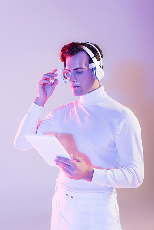 Cyborg in headphones holding digital tablet and adjusting eye lens on purple background