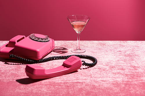 rose wine in glass near vintage phone on velour pink cloth isolated on pink, girlish concept