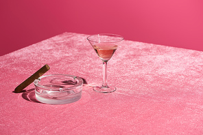 rose wine in glass near cigar on ashtray on velour pink cloth isolated on pink, girlish concept