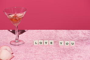 rose petals in glass near cubes with love you lettering on velour pink cloth isolated on pink, girlish concept
