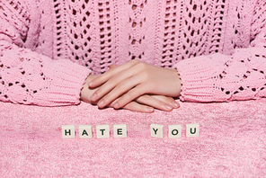 cropped view of woman in sweater near hate you lettering on pink velour cloth, girlish concept