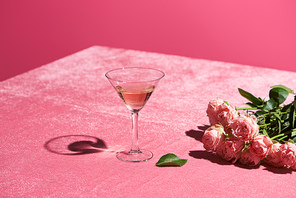 rose wine in glass near bouquet of roses on velour pink cloth isolated on pink, girlish concept