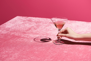 cropped view of woman holding glass of rose wine on velour cloth isolated on pink, girlish concept