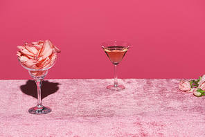 rose petals in glass near rose wine on velour pink cloth isolated on pink, girlish concept