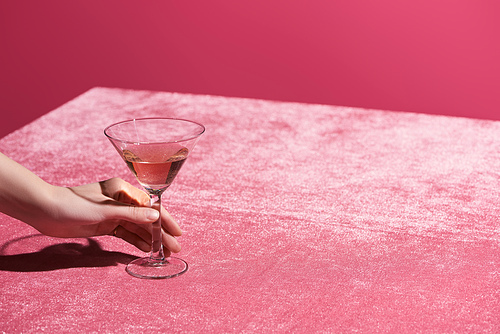 cropped view of woman holding glass of rose wine on velour cloth isolated on pink, girlish concept