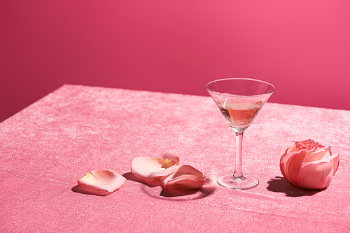rose wine in glass near petals and rose bud on velour pink cloth isolated on pink, girlish concept