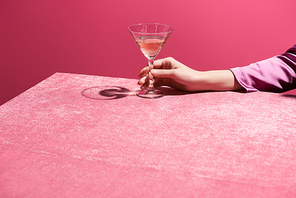 cropped view of woman holding glass of rose wine on velour cloth isolated on pink, girlish concept