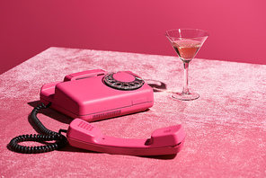 rose wine in glass near vintage phone on velour pink cloth isolated on pink, girlish concept