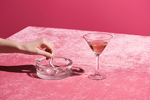 cropped view of woman putting out cigarette near glass of rose wine on velour cloth isolated on pink, girlish concept