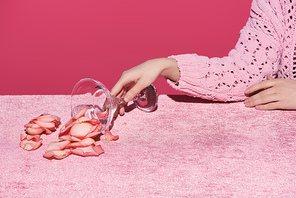 cropped view of woman with scattered petals from glass on velour cloth isolated on pink, girlish concept