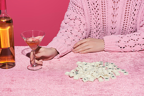 cropped view of woman holding glass of rose wine near cubes with letters on velour cloth isolated on pink, girlish concept