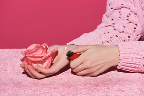 cropped view of woman holding rose and lighter on velour cloth isolated on pink, girlish concept