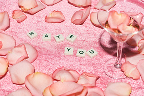 selective focus rose petals scattered near hate you lettering and glass on velour pink cloth, girlish concept