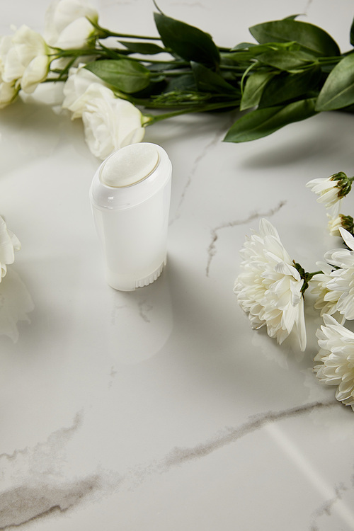 selective focus of roll on bottle of deodorant with flowers on white marble surface