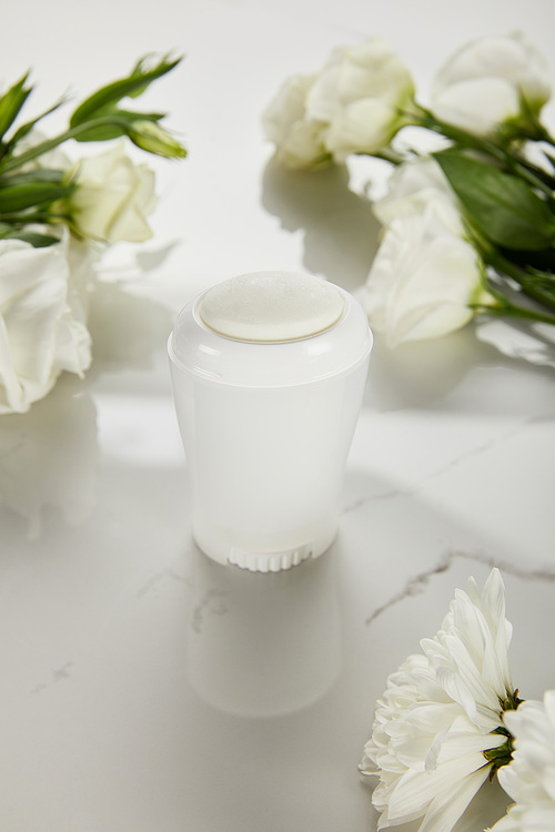 selective focus of roll on bottle of deodorant with flowers on white surface