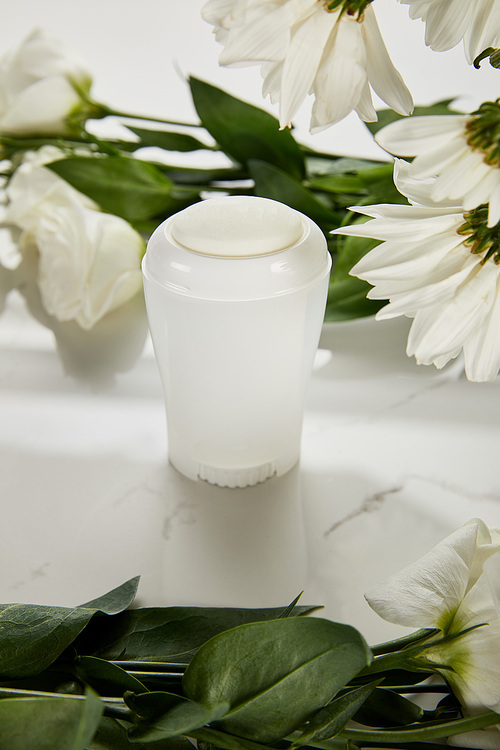 selective focus of roll on bottle of deodorant with flowers on white surface