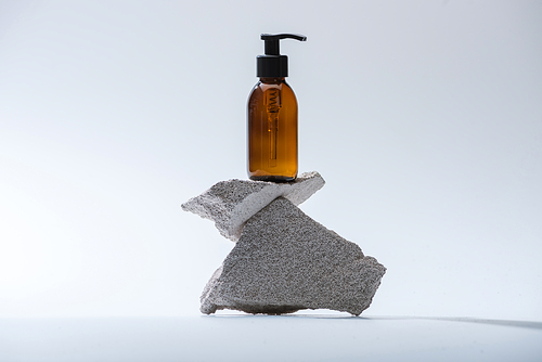 dispenser cosmetic bottle on stones on white background with back light