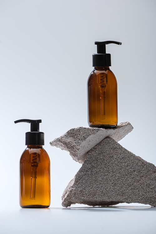 dispenser cosmetic bottles with stones on white background with back light