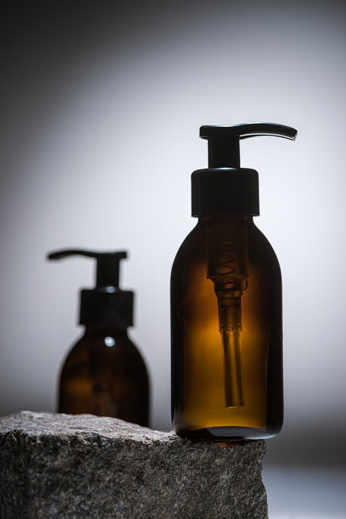 selective focus of dispenser cosmetic bottles on stone on dark background with back light
