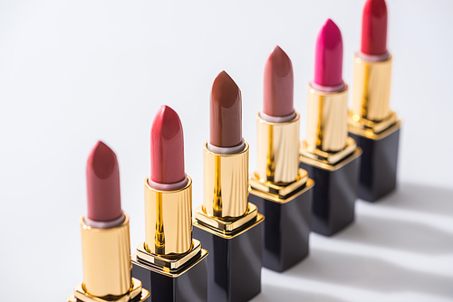 selective focus of assorted lipsticks in luxury tubes in line on white background