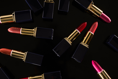 top view of assorted lipsticks in luxury tubes scattered isolated on black