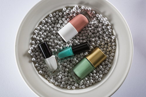 top view of assorted nail polish in bottles on plate with grey decorative beads