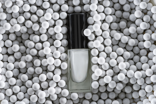 top view of white nail polish in bottle among grey decorative beads