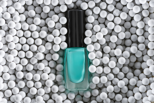 top view of blue nail polish in bottle among grey decorative beads
