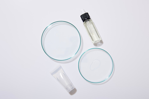 Top view of laboratory glassware, cosmetic tube and bottle of oil on grey background