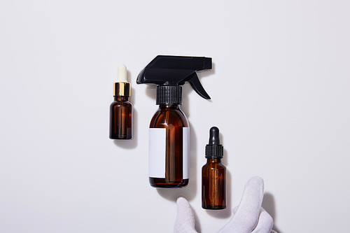 Cropped view of hand in glove with dispenser cosmetic bottles of oil on grey background
