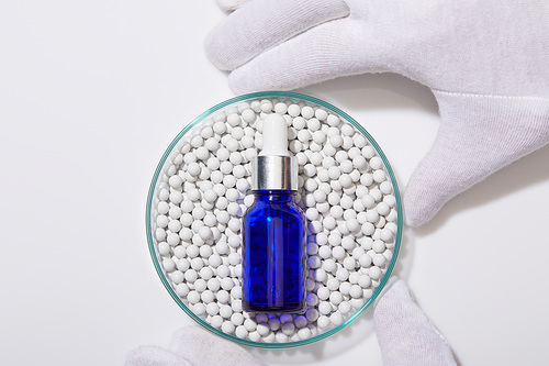 Cropped view of man holding laboratory glassware with blue bottle of oil on decorative beads on white background