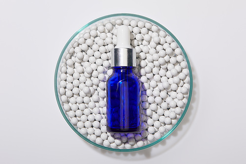 Top view of blue bottle of oil on decorative beads in laboratory glassware on white background