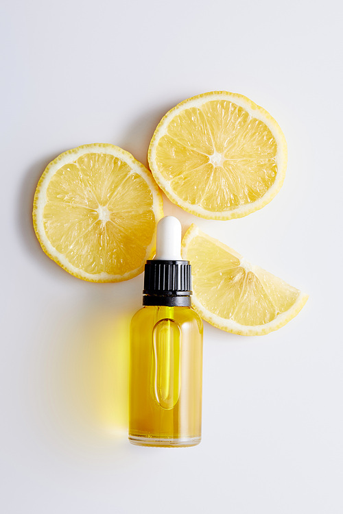 Top view of bottle of cosmetic oil with slices of lemon on white background