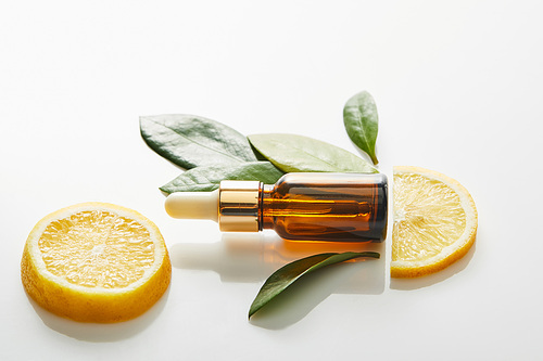 Top view of bottle of cosmetic oil with leaves and slices of lemon around on white background, panoramic shot