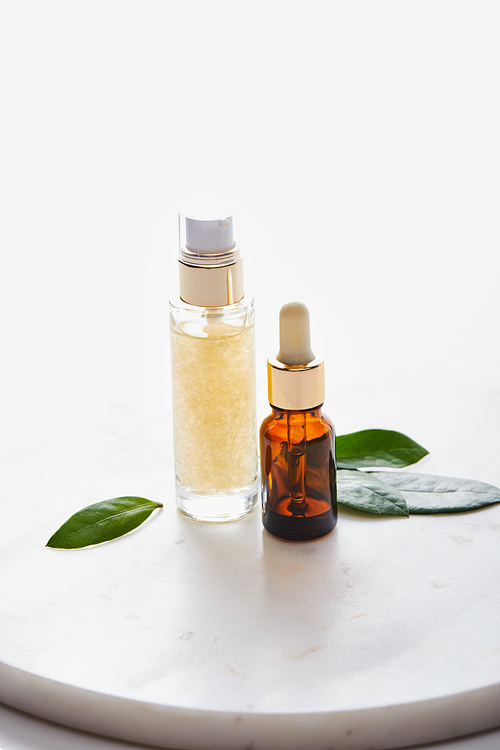 Bottles of cosmetic oil with leaves on round stand isolated on white