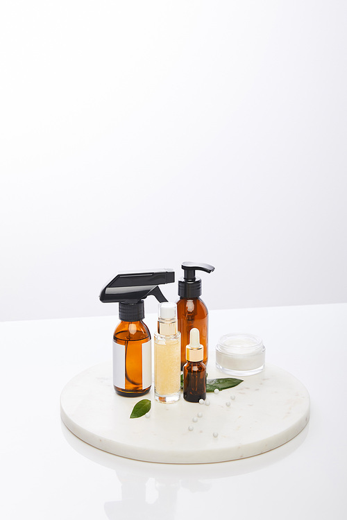 Dispenser bottles of oil next to cosmetic cream with plants, decorative beads on round stand isolated on grey