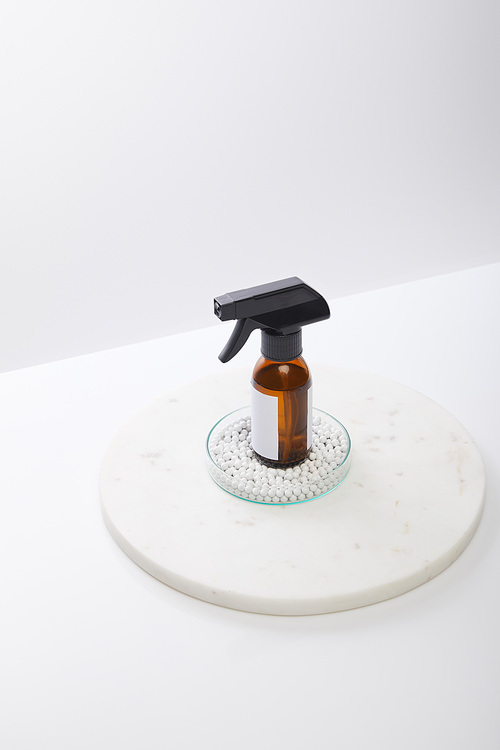 High angle view of dispenser bottle of cosmetic oil inside laboratory glassware with decorative beads isolated on grey