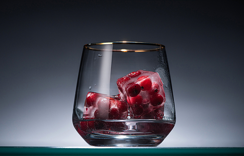 transparent glass with frozen redcurrant in ice cubes and vodka in dark with back light