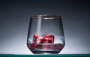 transparent glass with frozen redcurrant in ice cubes and vodka in dark with back light