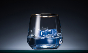 transparent glass with ice cubes and vodka in dark with blue back light