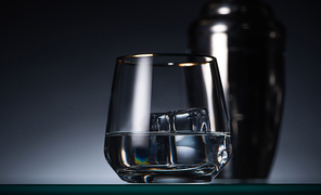 selective focus of transparent glass with ice cube and vodka in dark with back light and shaker