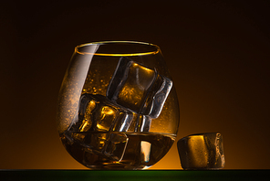 transparent glass with ice cubes and vodka in dark with warm back light
