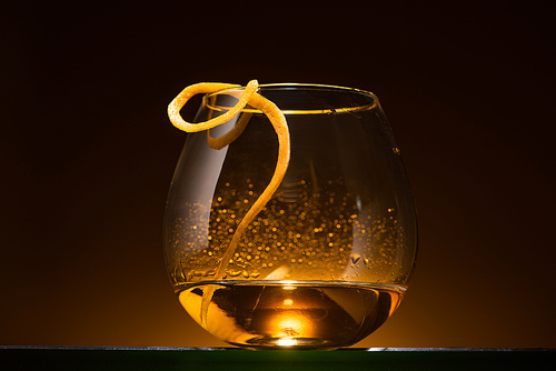 transparent glass with citrus peel and vodka in dark with warm back light