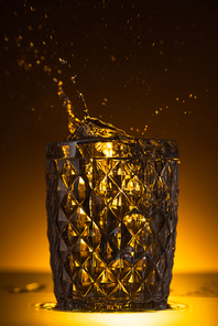 faceted glass with splashing vodka in dark with warm back light